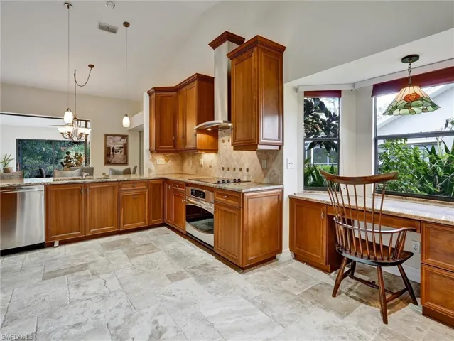 Kitchen featuring hanging light fixtures, brown cabinetry, light stone counters, backsplash, and stainless steel appliances
