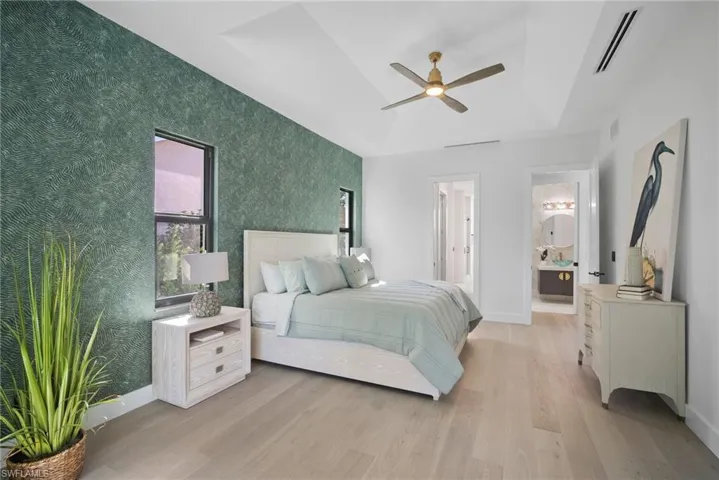 Bedroom featuring light wood-style floors, a ceiling fan, a raised ceiling, and wallpapered walls