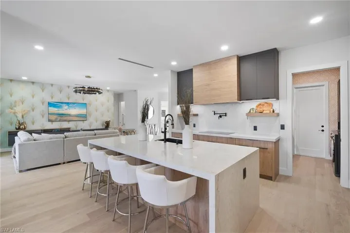 Kitchen with modern cabinets, light wood-style flooring, a breakfast bar, a kitchen island with sink, and light stone counters