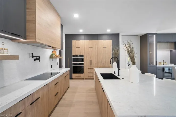 Kitchen featuring modern cabinets, light stone counters, recessed lighting, black appliances, and beverage cooler