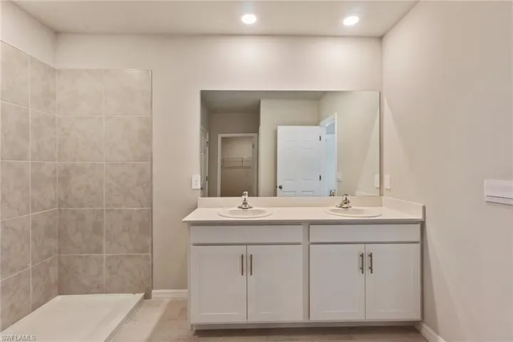Bathroom featuring double vanity, a walk in closet, and a tile shower