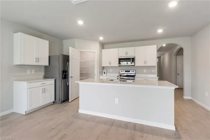Kitchen featuring arched walkways, white cabinetry, appliances with stainless steel finishes, an island with sink, and light wood-style floors