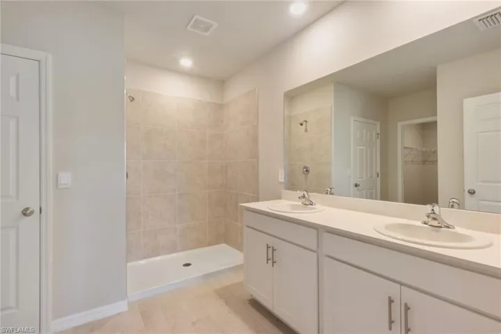 Bathroom featuring double vanity, a spacious closet, and a tile shower