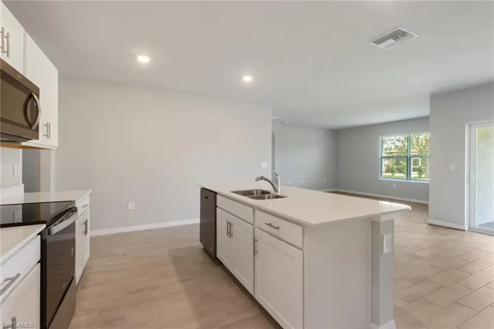 Kitchen featuring white cabinetry, stainless steel appliances, a center island with sink, open floor plan, and light stone countertops