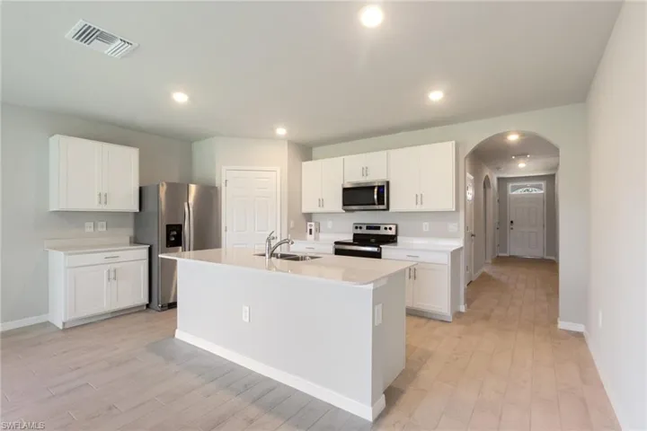 Kitchen featuring appliances with stainless steel finishes, a center island with sink, white cabinetry, light wood finished floors, and arched walkways