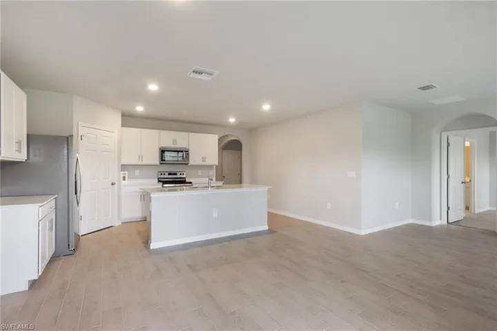 Kitchen with arched walkways, white cabinets, stainless steel appliances, a kitchen island with sink, and light wood-style floors