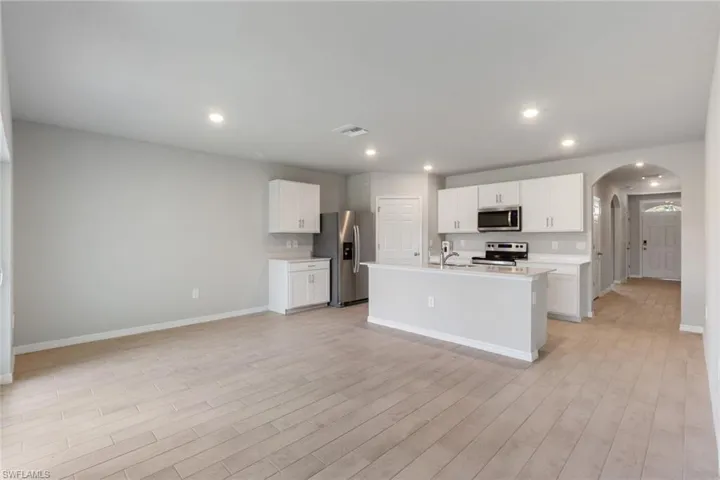 Kitchen featuring stainless steel appliances, arched walkways, white cabinets, recessed lighting, and a center island with sink