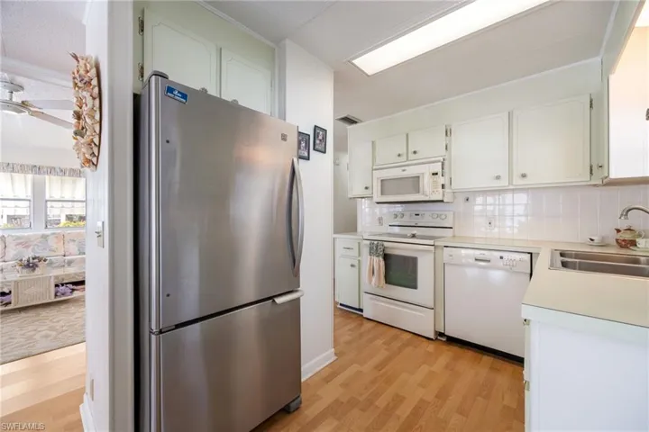 Kitchen featuring white appliances, decorative backsplash, light countertops, light wood-style flooring, and white cabinets