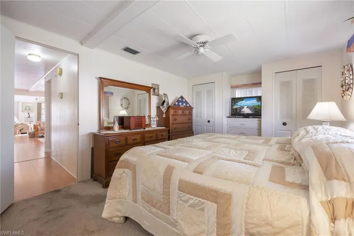 Carpeted bedroom with multiple closets, beam ceiling, and ceiling fan