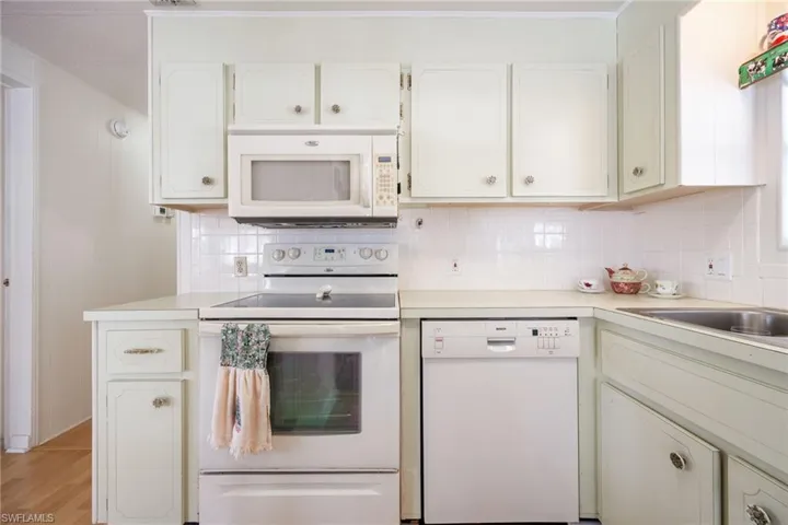 Kitchen featuring white appliances, light countertops, backsplash, and white cabinets