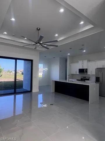 Open concept living area featuring large format tile flooring, a tray ceiling with recessed lighting, and a modern ceiling fan