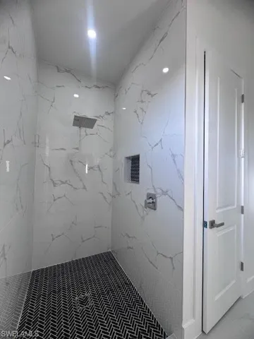 Walk-in shower featuring a rain showerhead, white marble-look wall tiling, recessed niche, and black herringbone mosaic floor tiling