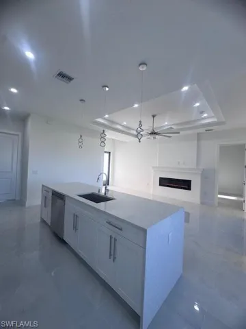 Spacious kitchen island featuring an undermount sink, stainless steel dishwasher, and light-toned countertop