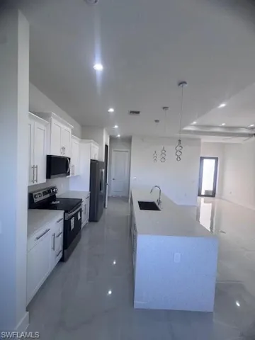 Modern kitchen featuring white shaker cabinetry, stainless steel appliances, and an expansive island with an undermount sink