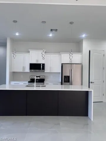 Contemporary kitchen featuring a large central island with a white countertop and dark cabinetry, white shaker-style perimeter cabinets, stainless steel appliances, and pendant lighting