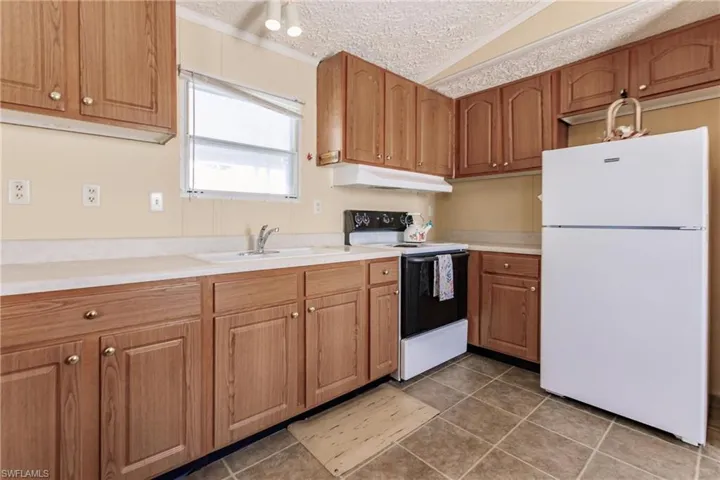 Kitchen featuring white appliances, lofted ceiling, tile patterned flooring, and sink