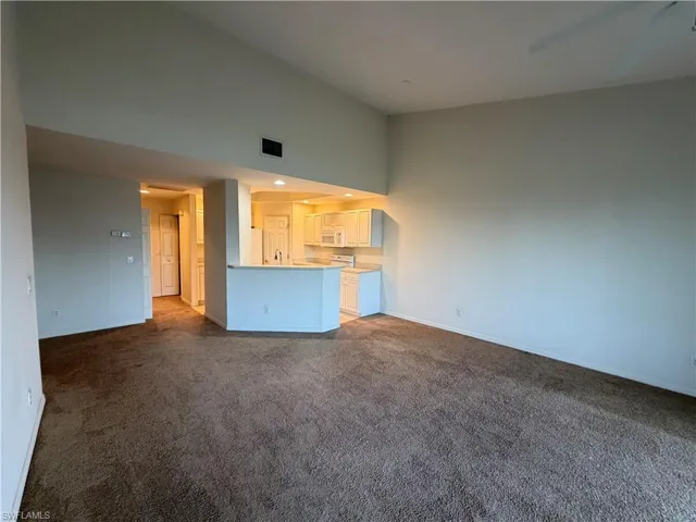 Unfurnished living room with a high ceiling, dark colored carpet, and recessed lighting