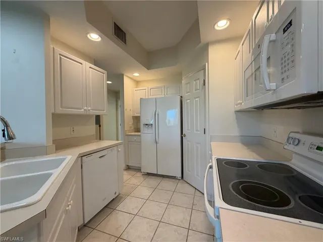 Kitchen featuring white appliances, light countertops, white cabinets, recessed lighting, and light tile patterned flooring
