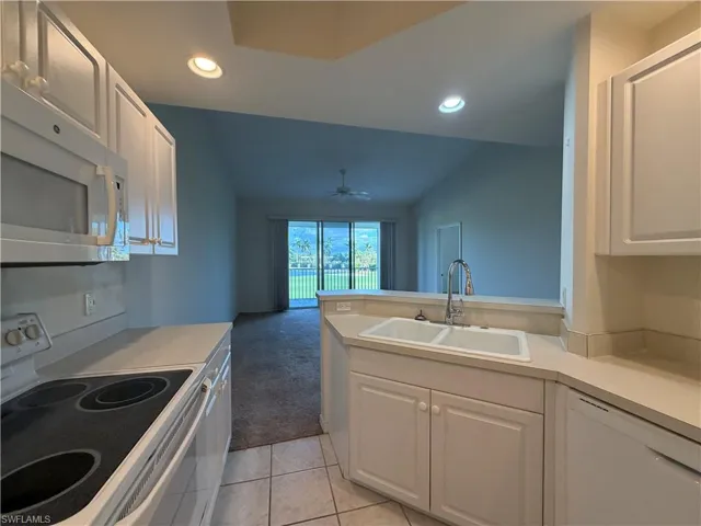 Kitchen featuring white appliances, white cabinets, light countertops, light colored carpet, and recessed lighting