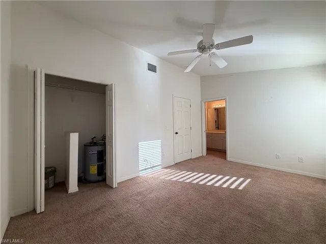 Unfurnished bedroom featuring lofted ceiling, water heater, ensuite bathroom, a ceiling fan, and a closet
