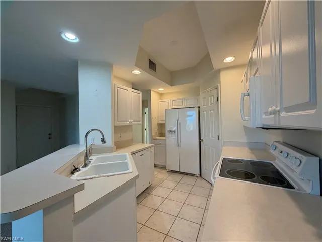 Kitchen featuring a peninsula, white appliances, light countertops, white cabinets, and recessed lighting