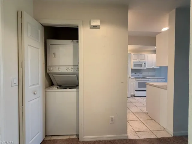Laundry area with stacked washing machine and dryer and light tile patterned floors