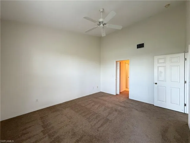 Unfurnished bedroom featuring dark colored carpet, ceiling fan, and a high ceiling