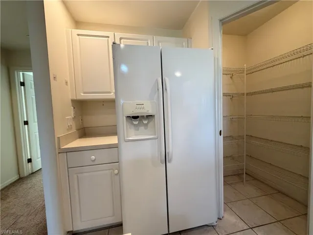 Kitchen with white fridge with ice dispenser, white cabinetry, and light countertops