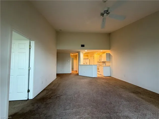 Unfurnished living room featuring dark carpet, ceiling fan, a high ceiling, and arched walkways