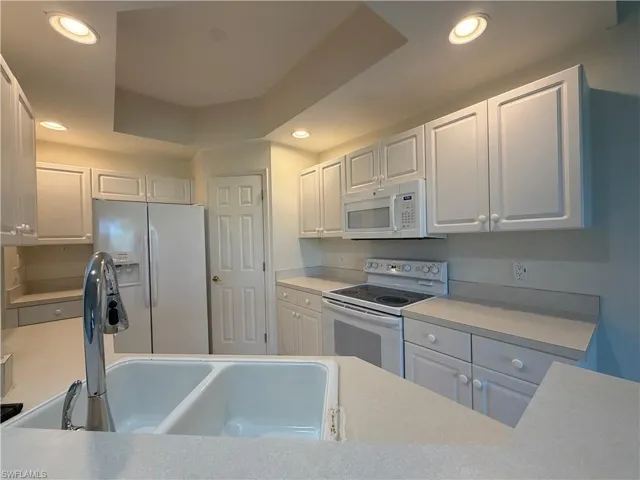 Kitchen featuring white appliances, light countertops, white cabinets, recessed lighting, and a raised ceiling