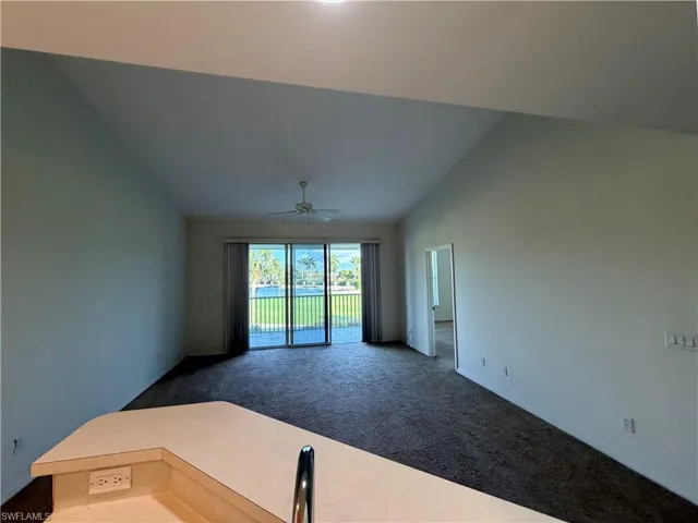 Unfurnished room with dark colored carpet, lofted ceiling, and a ceiling fan