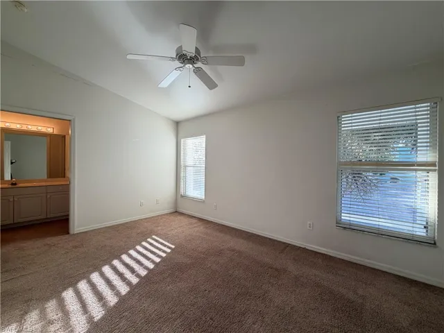 Unfurnished bedroom with lofted ceiling, dark carpet, ceiling fan, and ensuite bathroom