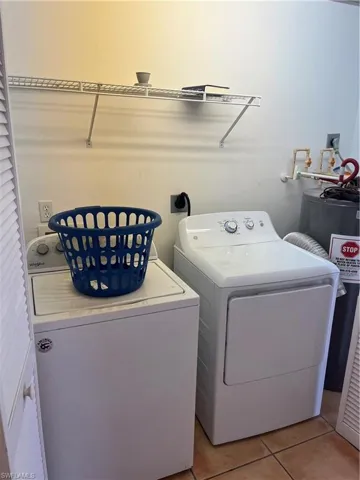 Clothes washing area featuring water heater, hookup for an electric dryer, washer and clothes dryer, and light tile floors