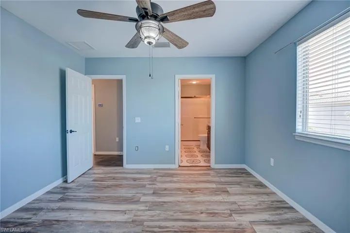 Unfurnished bedroom with light wood-style flooring, ensuite bath, and ceiling fan