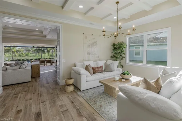Living room with hardwood / wood-style floors, beam ceiling, a chandelier, ornamental molding, and coffered ceiling