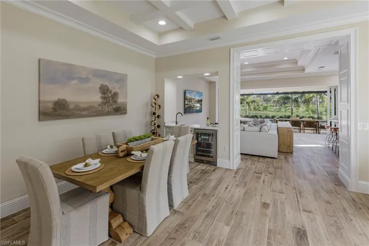 Dining space featuring light hardwood / wood-style flooring, wine cooler, ornamental molding, and coffered ceiling