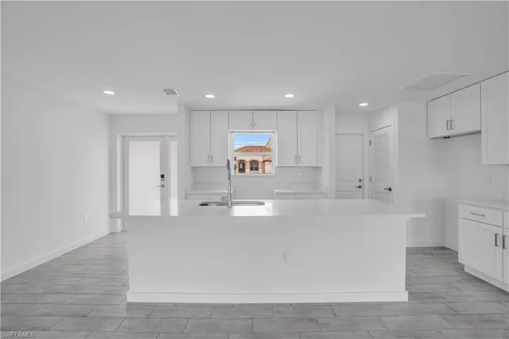 Modern kitchen featuring an expansive island with a countertop sink, white cabinetry with contemporary hardware, light-toned backsplash, recessed lighting, and tile flooring