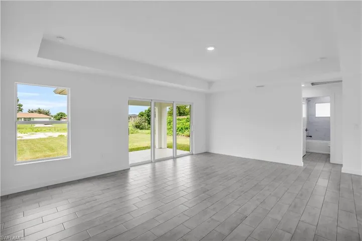 Spacious room featuring light gray wood-finish flooring, a tray ceiling with recessed lighting, and large sliding glass doors providing access to the exterior