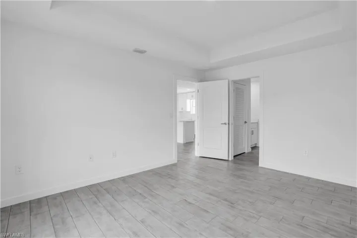 Spacious interior featuring light wood-finish flooring, a tray ceiling, and white baseboards