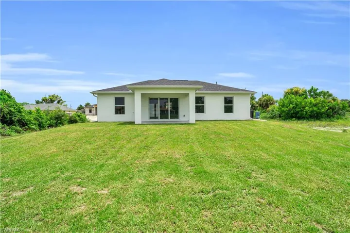 Expansive green lawn with a white stucco exterior featuring a covered patio and sliding glass doors