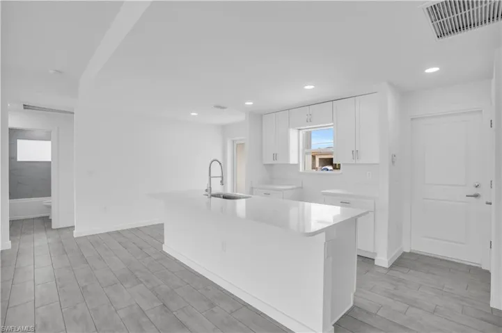 Open-concept kitchen featuring an island with a stainless steel sink and modern faucet, white cabinetry, integrated recessed lighting, and wood-finish flooring
