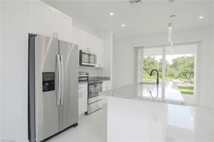 Kitchen with sink, stainless steel appliances, pendant lighting, a kitchen island with sink, and white cabinets