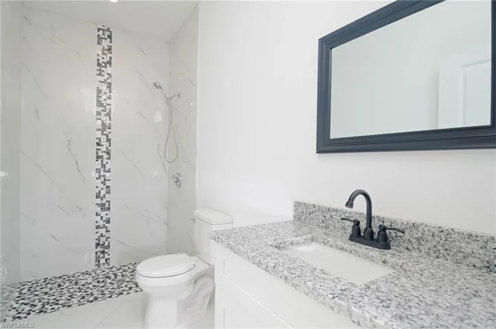 Bathroom featuring a tile shower, vanity, and toilet