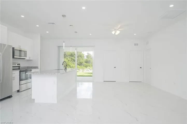 Kitchen with light stone countertops, appliances with stainless steel finishes, ceiling fan, a center island with sink, and white cabinetry