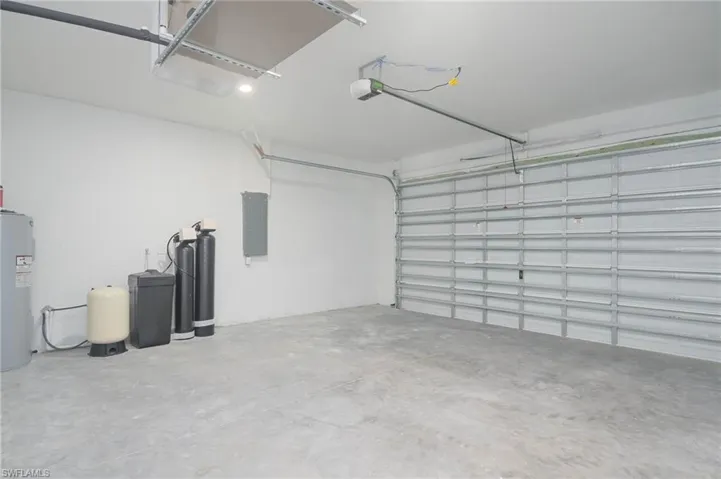 Garage with electric water heater, electric panel, and a garage door opener
