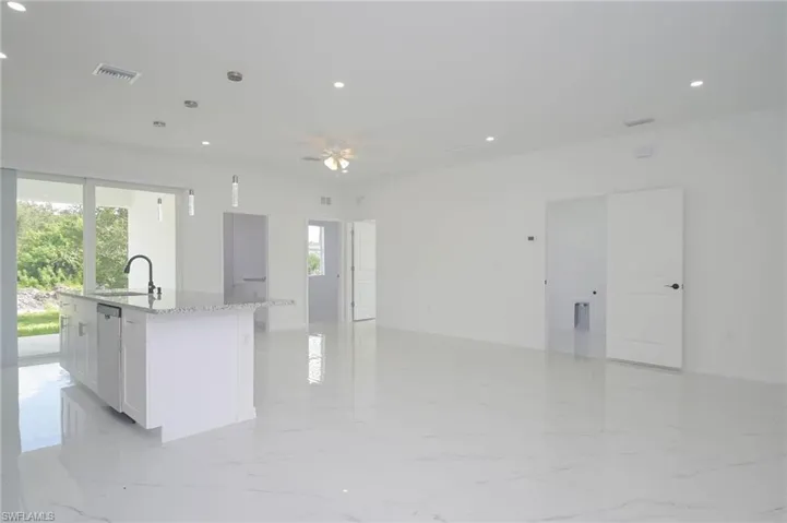 Kitchen with dishwasher, white cabinets, light stone countertops, an island with sink, and decorative light fixtures