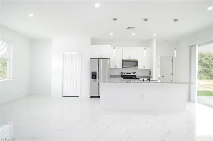 Kitchen featuring pendant lighting, white cabinetry, stainless steel appliances, and a kitchen island with sink