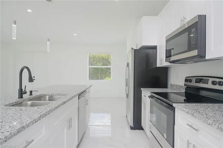 Kitchen with sink, light stone counters, pendant lighting, white cabinets, and appliances with stainless steel finishes
