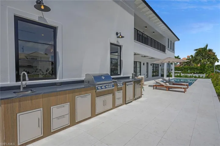 Outdoor summer kitchen at this Marco Island luxury waterfront home featuring built-in grill, beer tap, refrigerator, double side burner, and seating area beside the saltwater pool.