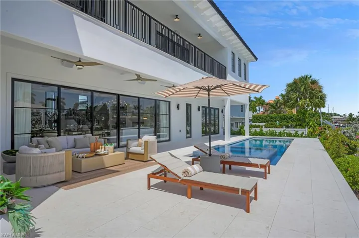 Poolside view of Marco Island luxury home featuring saltwater infinity spa, two lounge chairs with umbrella, and additional outdoor seating for entertaining.